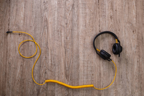 Headphones with yellow cable. Wooden background. - Foto, afbeelding