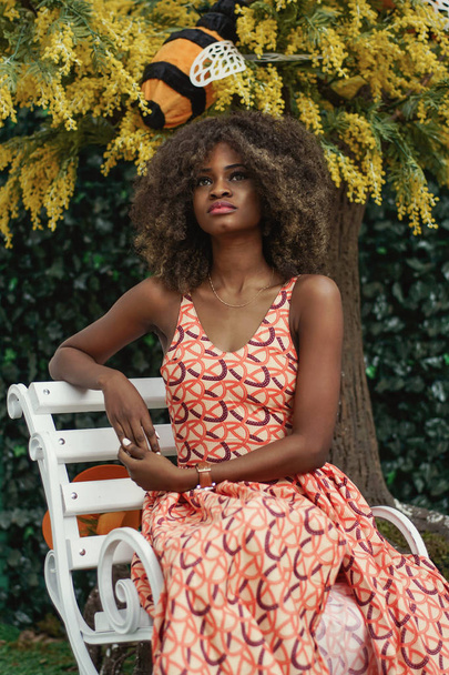 Pretty serious afro american girl sitting on a while bench. - Photo, Image