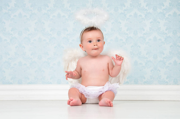 Little angel smiling and sitting on the floor. - Фото, изображение
