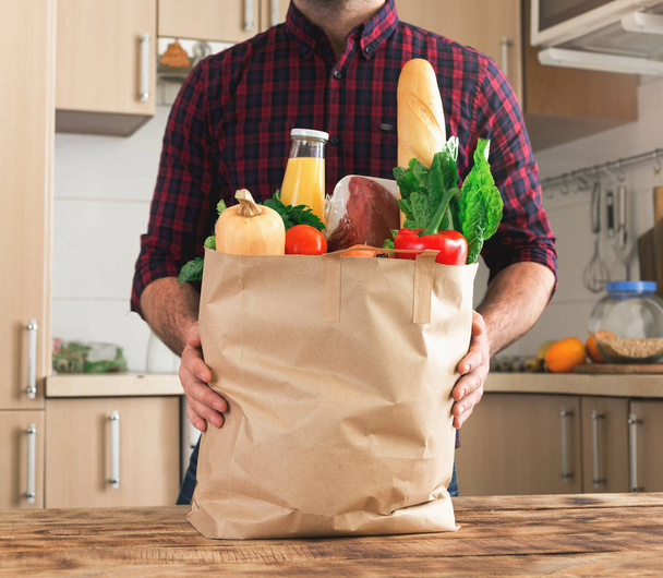 Man holding paper bag of healthy food on wooden table - Fotó, kép