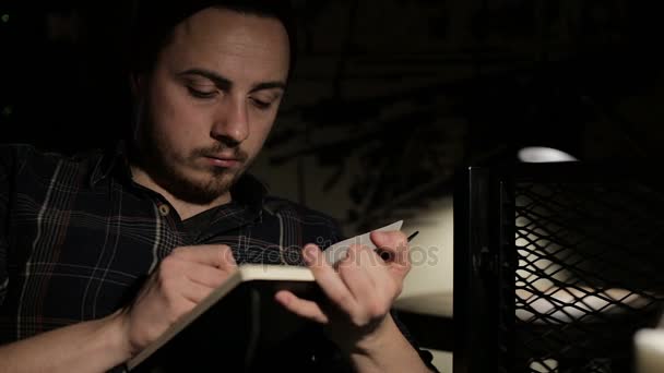 Young man makes a sketch in a notebook at night in a bar - Video, Çekim