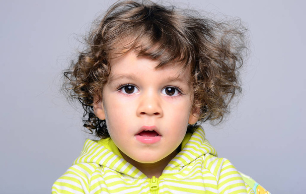 Portrait of a beautiful boy with long curly hair. Toddler looking surprised and playing  - Valokuva, kuva