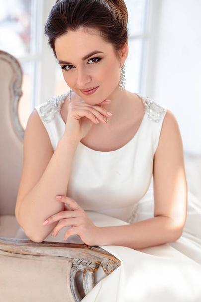 close-up portrait of beautiful brunette bride with elegant hairstyle and makeup wearing long luxury wedding dress - Fotó, kép