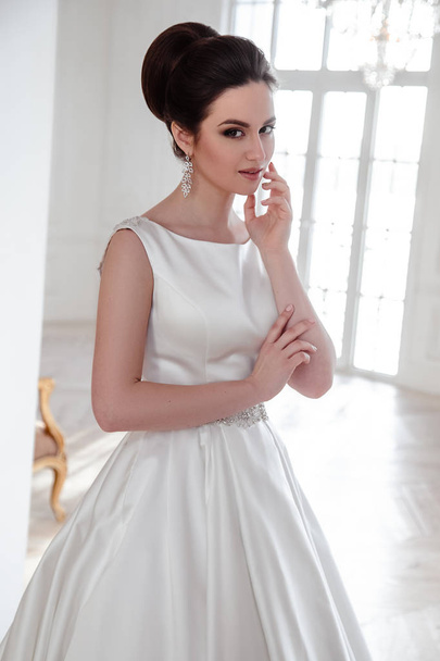 portrait of beautiful brunette bride with elegant hairstyle and makeup wearing long luxury wedding dress - Fotó, kép