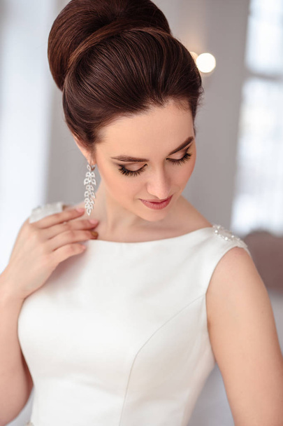 close-up portrait of beautiful brunette bride with elegant hairstyle and makeup wearing long luxury wedding dress - Fotó, kép