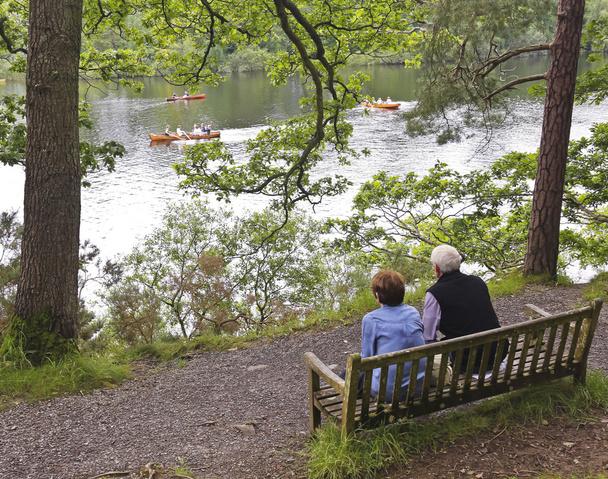 Ein älteres Ehepaar beobachtet Ruderboote in einem See - Foto, Bild