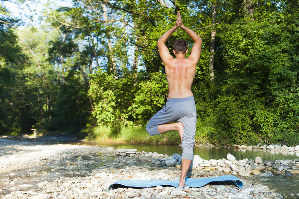 Człowiek, medytując niedaleko rzeki górskie. Joga praktykujących na zewnątrz - Zdjęcie, obraz