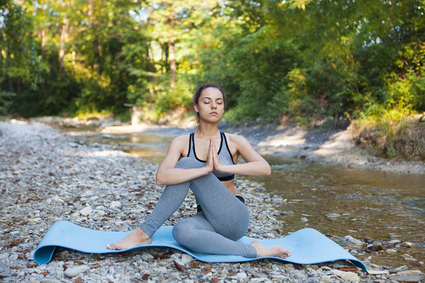Young woman meditating near the mountain river. Yoga practicing  - Photo, image