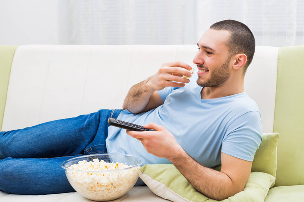 Мужчина смотрит телевизор и ест попкорн
 - Фото, изображение