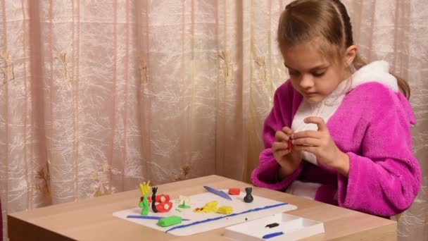 Girl sculpts crafts from plasticine sitting at a table on the other side of the empty space under the title - Footage, Video