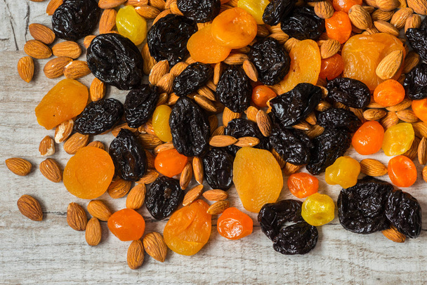 prunes, dried apricots, dried mandarins and almonds on a light wooden background - Foto, Bild