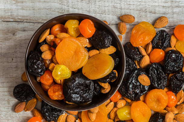 prunes, dried apricots, dried mandarins and almonds in a bowl on a light wooden background - Photo, Image