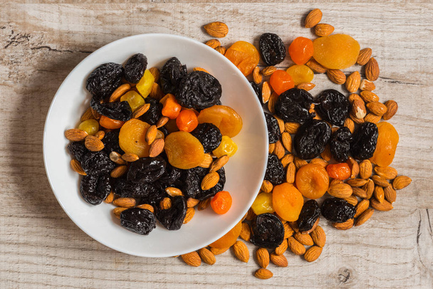 prunes, dried apricots, dried mandarins and almonds in a bowl on a light wooden background - Photo, Image