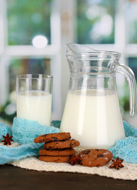Pitcher and glass of milk with cookies on crewnecks knitwear on wooden table on window background - Фото, зображення