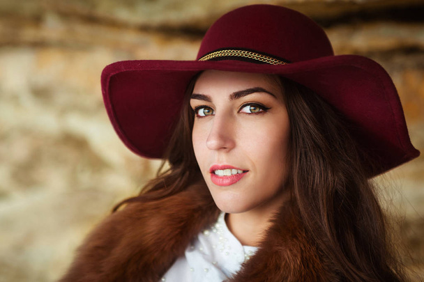 Beautiful girl in maroon felt hat close up portrait. Outdoor shoot. look at the camera. - 写真・画像