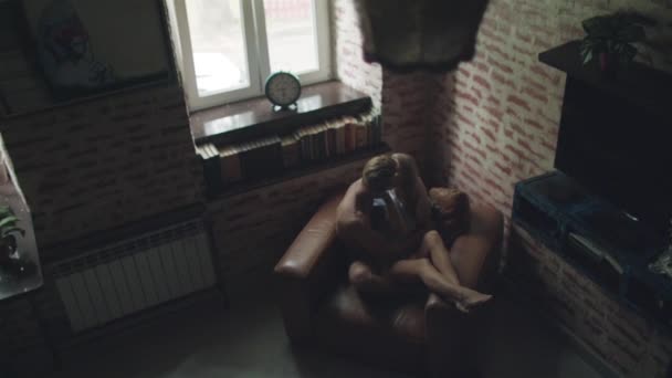 Пара влюбленных поцелуев в помещении, сидящих в кресле с видом сверху. Молодой человек и женщина обнимаются дома, обнимая друг друга крепко. Интимный момент близости друг с другом
 - Кадры, видео