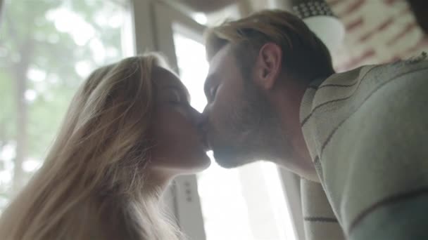 Kissing at light window backlit background close up slow motion. Young man comes to kiss blonde girlfriend waiting for him at home autumn morning weekend. Romantic couple relationship sincere emotions - Footage, Video