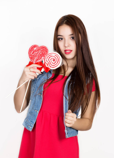 beautiful young woman dressed in a red dress holding a lollipop, studio shot - Foto, Imagem