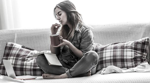 Witte gezellig bed en een mooi meisje met een computer en een boek, het drinken van een warme drank, concepten van huis en comfort - Foto, afbeelding