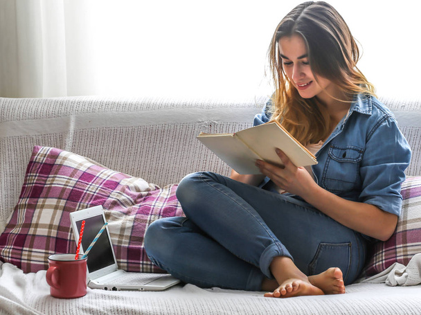 Blanco acogedora cama y una hermosa chica con un ordenador y un libro, beber una bebida caliente, conceptos de hogar y comodidad
 - Foto, imagen
