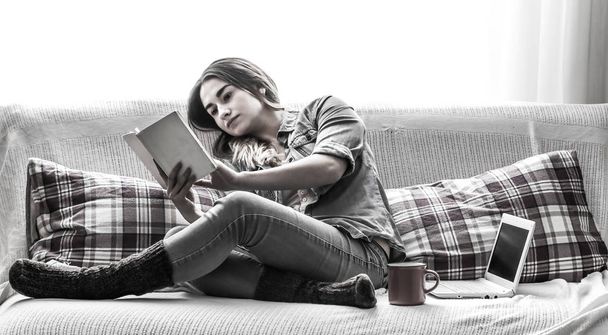Blanco acogedora cama y una hermosa chica con un ordenador y un libro, beber una bebida caliente, conceptos de hogar y comodidad
 - Foto, Imagen