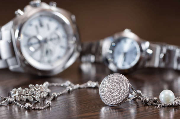 Anelli in argento e catena sdraiato su sfondo orologi cromati
 - Foto, immagini