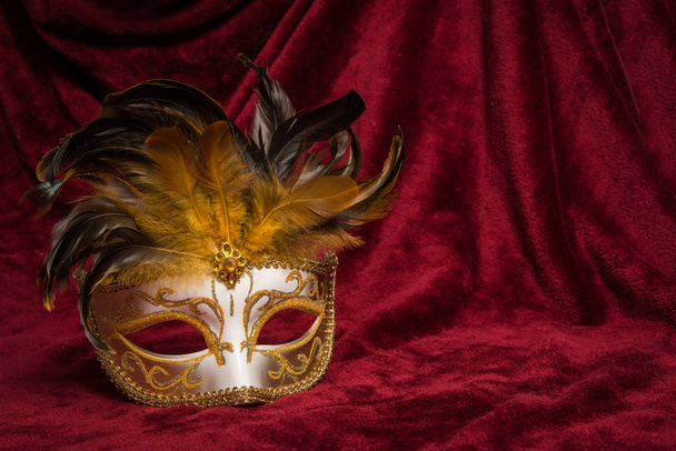 Masque de carnaval vénitien doré marron sur un rideau de velours rouge drapé
 - Photo, image