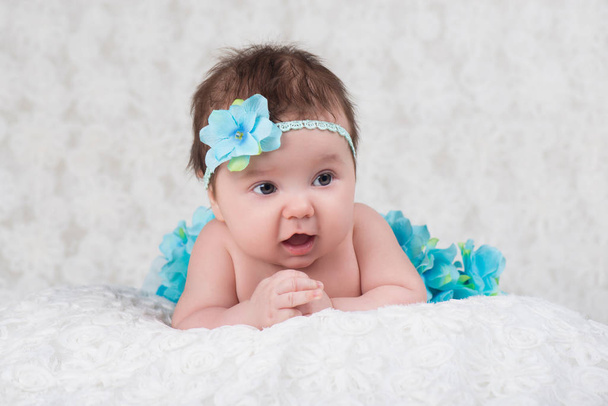 neugeborenes Porträt eines Mädchens mit einem Verband, das eine blaue Blume strickt - Foto, Bild