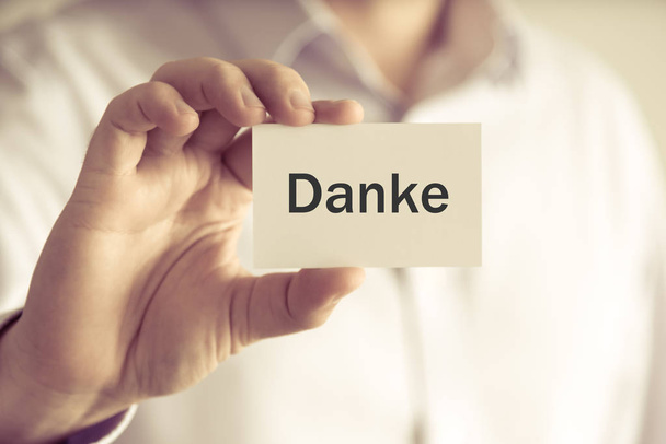 Бизнесмен с карточкой "DANKE" на немецком языке - перевод: СПАСИБО
 - Фото, изображение