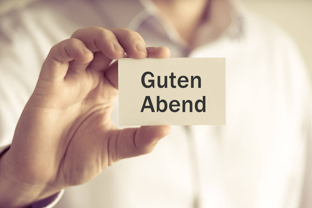 Zakenman holding tekstkaartje "Guten Abend" geschreven in het Duits - Vertaling: Goedenavond - Foto, afbeelding