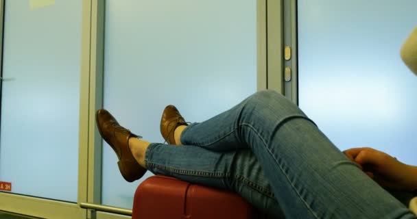 Frau wartet mit überkreuzten Beinen auf Gepäcktasche in moderner Flughafenterminal-Lounge - Filmmaterial, Video