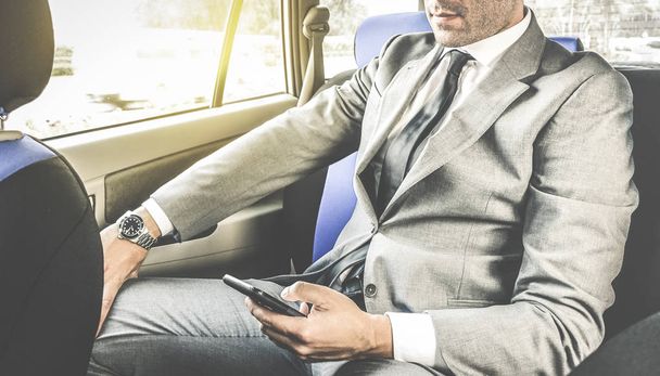 Young handsome businessman sitting in taxi cab while texting sms with smartphone - Business concept with modern man using smart phone - Soft vintage editing with artificial sunlight from window - Photo, Image