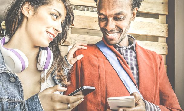 Multiracial couple flirting with smartphone numbers - Modern concept of mobile phone technology with happy people having fun - City urban lifestyle - Retro filter with focus on girl - Foto, imagen