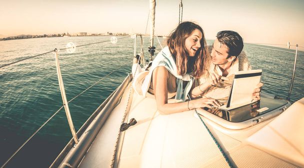 Young couple in love on sail boat having fun with tablet - Happy luxury lifestyle on yacht sailboat - Technology interaction with satellite wifi connection - Retro contrasted filter - Photo, Image