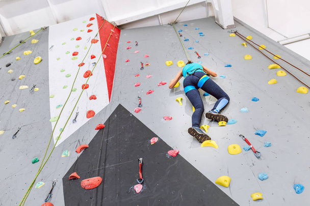Jonge vrouw klimmen op praktijk muur van binnenshuis gym, achteraanzicht - Foto, afbeelding