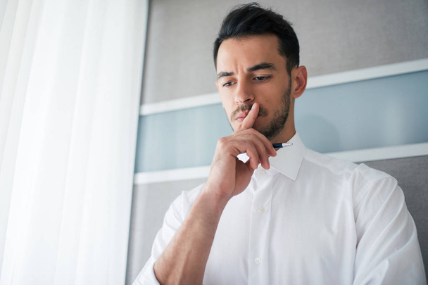 Thinking handsome businessman in white shirt with a finger on the mouth looking down. Business. Bottom view. - Photo, Image
