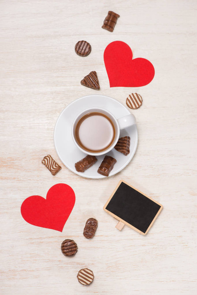 Φόντο ημέρα του Αγίου Βαλεντίνου με μπάλες σοκολάτας, φλιτζάνι καφέ, κόκκινες καρδιές και σημειωματάριο - Φωτογραφία, εικόνα