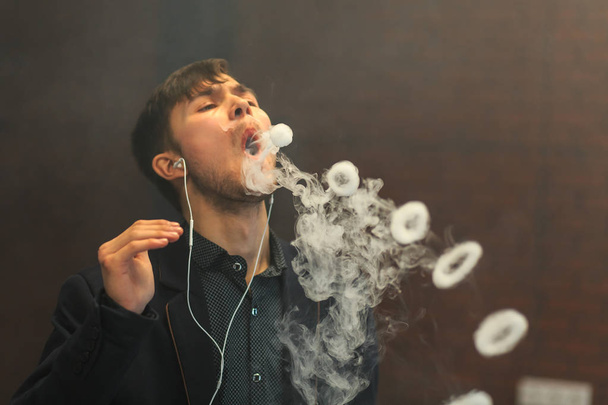 Young handsome white guy let rings out of steam. Vaping. - Zdjęcie, obraz