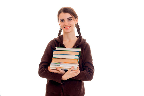 молода щаслива брюнетка студентська дівчина в коричневому спортивному одязі з кісками та книгами в руках посміхається на камеру ізольовано на білому тлі
 - Фото, зображення