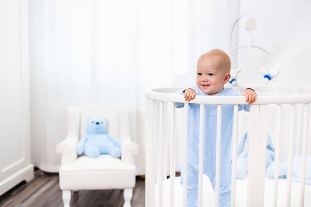 Babyjongen permanent in bed in witte kinderkamer - Foto, afbeelding