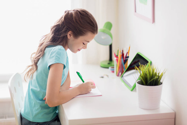 girl with tablet pc writing to notebook at home - Photo, image