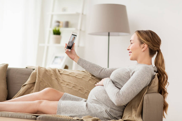 pregnant woman taking smartphone selfie at home - 写真・画像