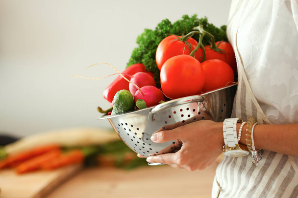 Young woman holding vegetables standing in kitchen - Foto, immagini