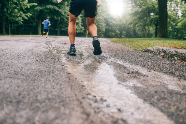 Muscular calves of fit male jogger training for cross country forest trail race in the rain on a nature trail. - Foto, imagen