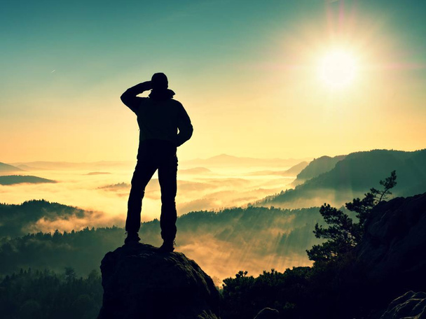 Männersilhouette, die hoch auf Klippen klettert. Wanderer erklimmt Gipfel und genießt Aussicht. - Foto, Bild