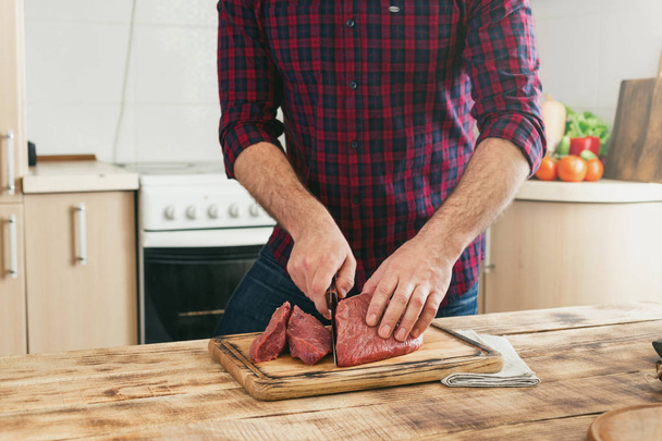 Man cuts of beef meat on a wooden cutting board - Фото, изображение