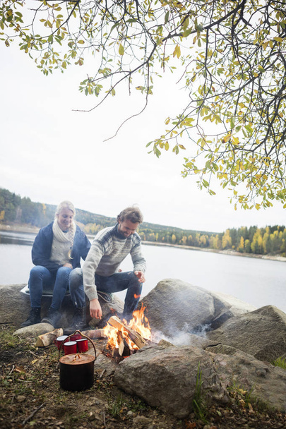 Couple Sitting Near Bonfire On Lakeshore - Фото, изображение