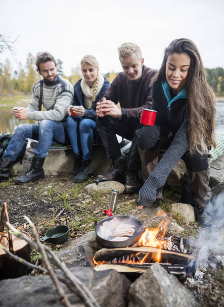 Woman Cooking Food On Campfire With Friends In Background - Foto, imagen