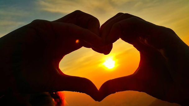Женские руки в форме сердца против драматического восхода солнца
 - Фото, изображение