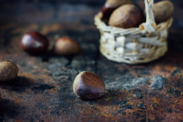 Fresh chestnuts in basket over black rustic surface. - Фото, изображение